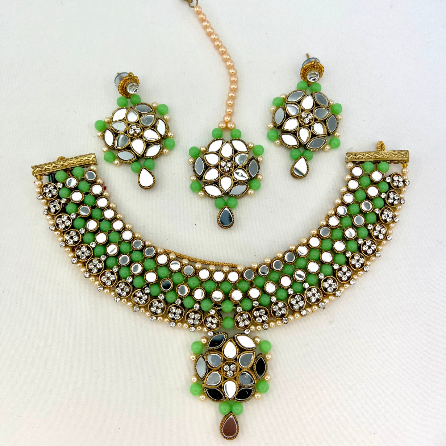 Mirror necklace set with green beads, clear stones and pearls. Set includes, necklace, tikka and earrings. Prefect for Indian weddings, parties and special occasions. Latest 2022 fashion. High end Indian fashion jewellery with top quality stones and beads.
